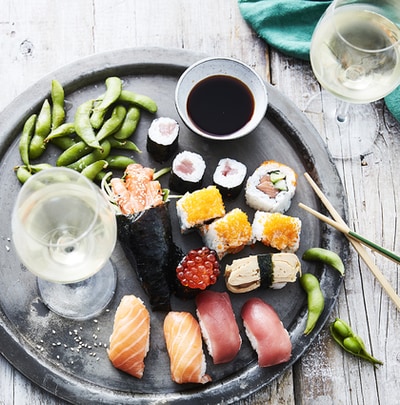 Schaal met verschillende soorten sushi en een glas witte wijn